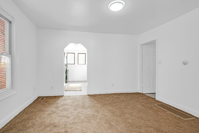 unfurnished room with carpet flooring, baseboards, visible vents, and arched walkways