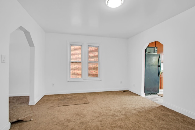 unfurnished room featuring baseboards, arched walkways, and carpet