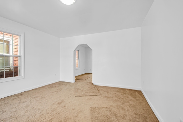 carpeted empty room featuring baseboards and arched walkways