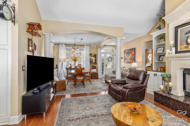 living room featuring vaulted ceiling, a fireplace, wood finished floors, arched walkways, and ornate columns