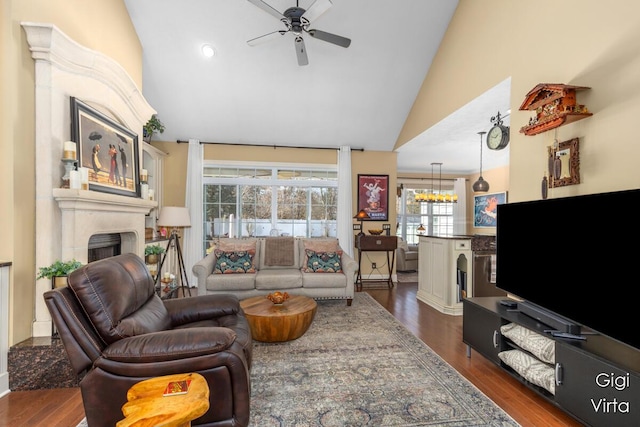 living room with ceiling fan with notable chandelier, dark wood-style floors, a fireplace, and high vaulted ceiling