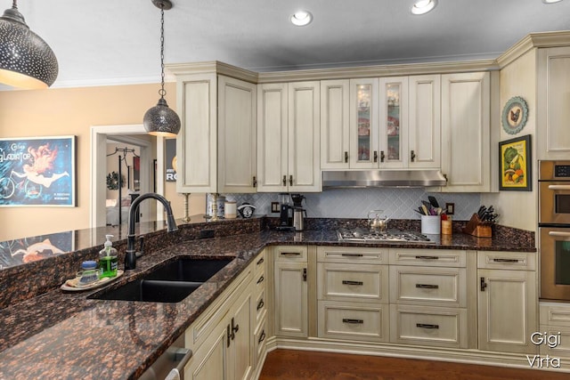 kitchen with tasteful backsplash, under cabinet range hood, cream cabinetry, stainless steel appliances, and a sink