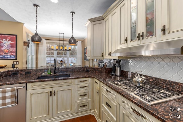 kitchen featuring a sink, under cabinet range hood, cream cabinets, stainless steel appliances, and hanging light fixtures