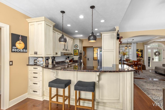 kitchen with dark wood-type flooring, ornamental molding, cream cabinets, arched walkways, and a peninsula