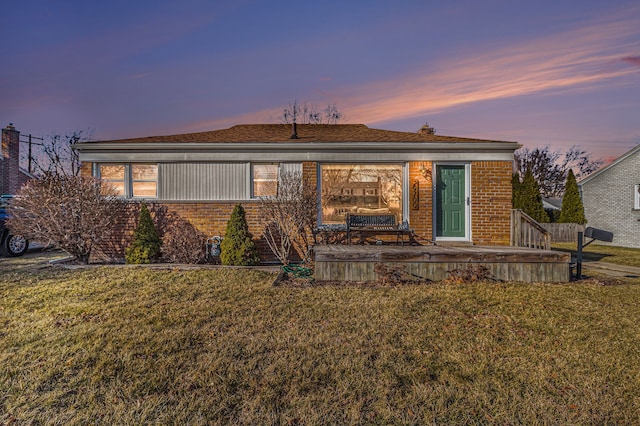 back of property at dusk featuring a lawn and brick siding