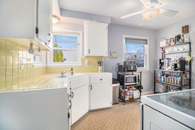 kitchen with a ceiling fan, a sink, tile countertops, white cabinets, and decorative backsplash