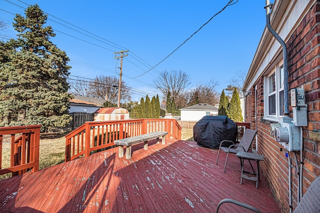 deck with an outbuilding, a grill, a storage shed, and fence