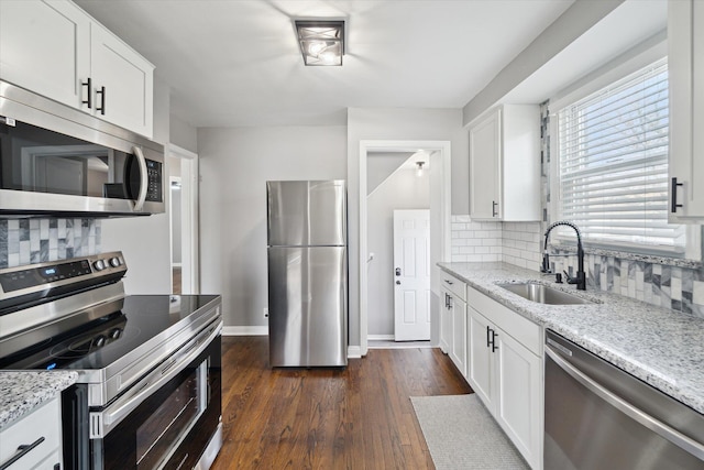 kitchen featuring light stone counters, a sink, stainless steel appliances, dark wood-type flooring, and white cabinets