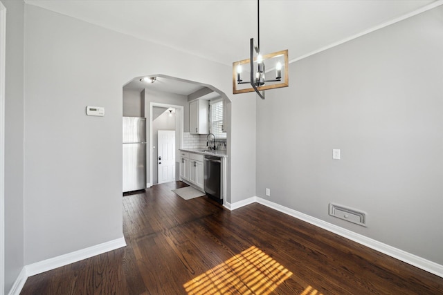 unfurnished dining area with a sink, baseboards, arched walkways, and dark wood-style floors