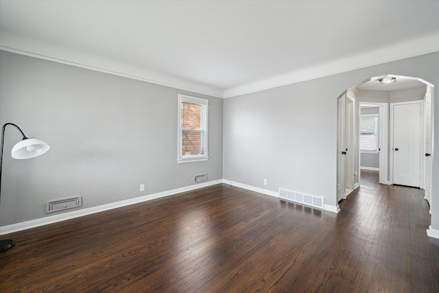 unfurnished room featuring visible vents, arched walkways, baseboards, and dark wood finished floors