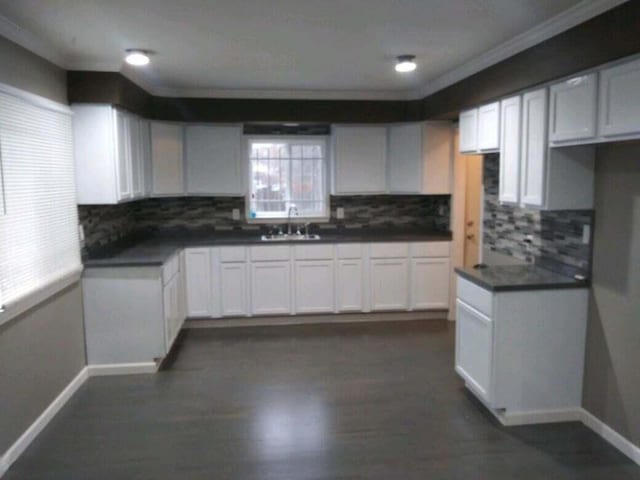 kitchen featuring tasteful backsplash, dark countertops, baseboards, white cabinetry, and a sink