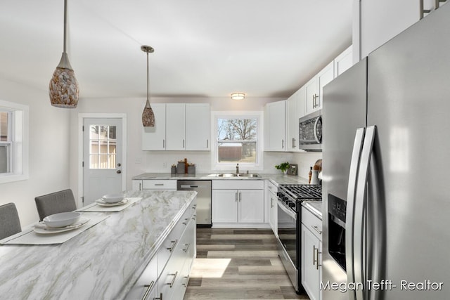 kitchen featuring light stone counters, wood finished floors, stainless steel appliances, white cabinets, and backsplash