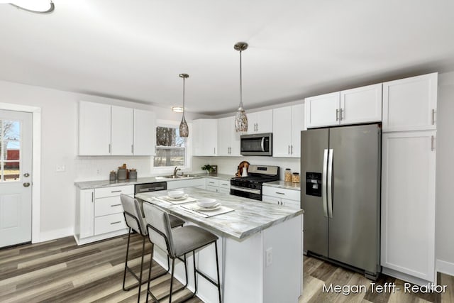 kitchen featuring hanging light fixtures, white cabinets, stainless steel appliances, and wood finished floors