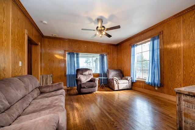 living area with a wealth of natural light, wood finished floors, ceiling fan, and ornamental molding