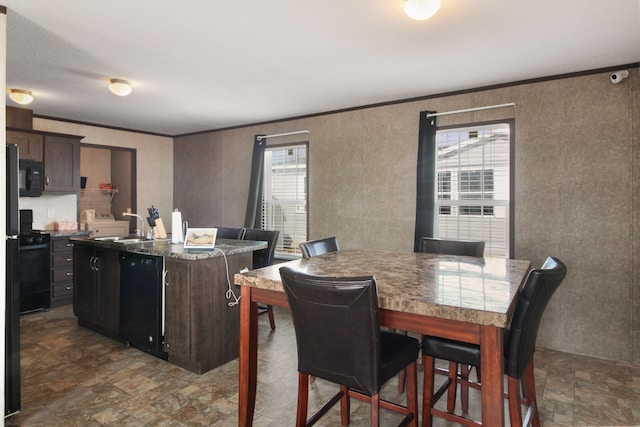 kitchen with a kitchen island with sink, stone finish flooring, dark brown cabinetry, black appliances, and a sink