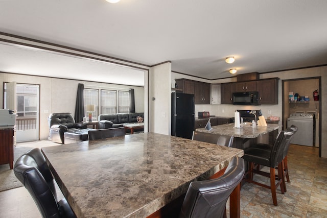 kitchen with dark brown cabinets, a kitchen bar, washer / dryer, black appliances, and a kitchen island with sink