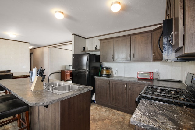 kitchen with dark countertops, dark brown cabinets, a breakfast bar area, freestanding refrigerator, and a sink