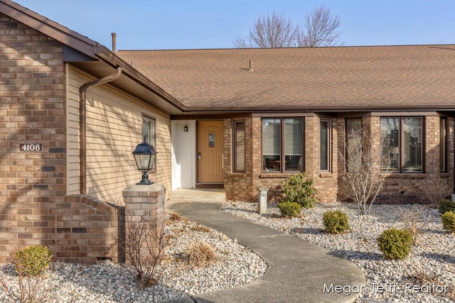 property entrance featuring brick siding and a shingled roof