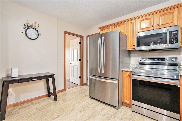 kitchen with a textured ceiling, stainless steel appliances, light wood-type flooring, and baseboards