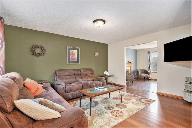 living room featuring a fireplace, a textured ceiling, baseboards, and wood finished floors