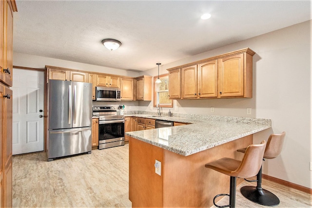 kitchen featuring a kitchen bar, light stone counters, appliances with stainless steel finishes, a peninsula, and light wood finished floors