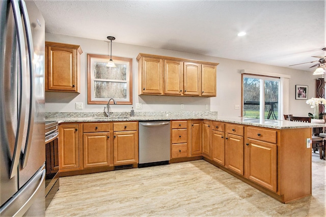 kitchen with light stone countertops, pendant lighting, a peninsula, stainless steel appliances, and a sink