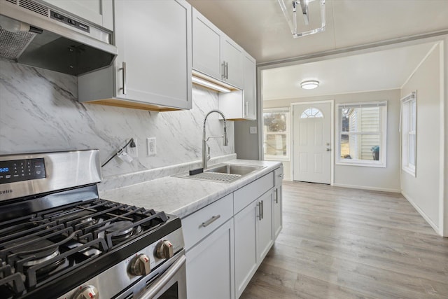 kitchen with light wood finished floors, tasteful backsplash, under cabinet range hood, stainless steel range with gas stovetop, and a sink