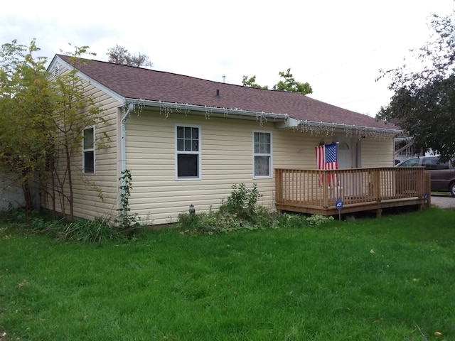 rear view of house with a deck, a yard, and a shingled roof