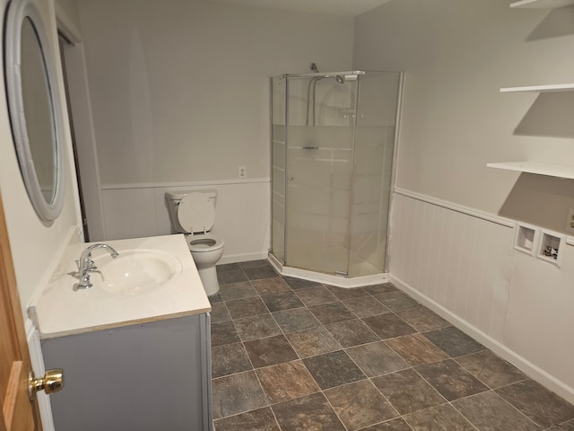 bathroom featuring toilet, a stall shower, stone finish floor, wainscoting, and vanity