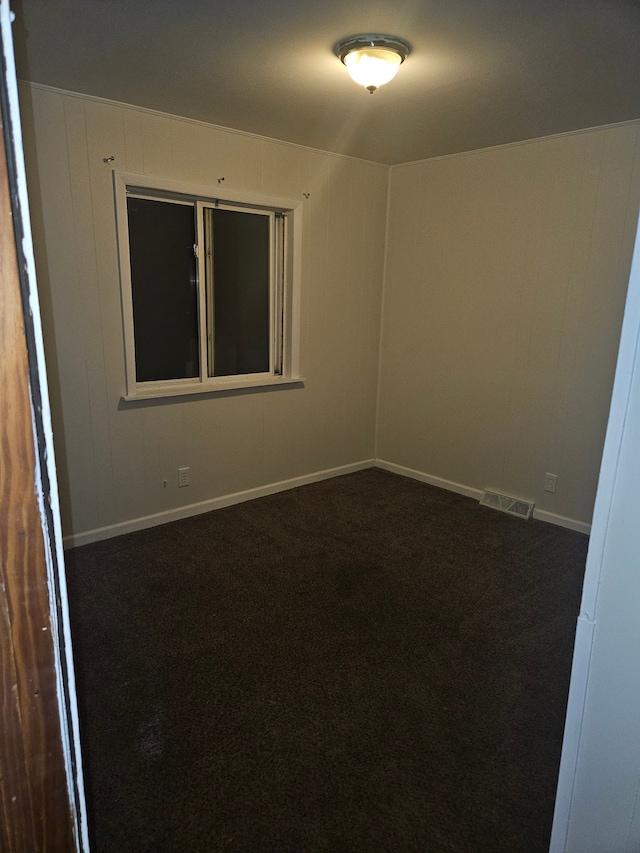 spare room featuring visible vents, baseboards, and dark carpet