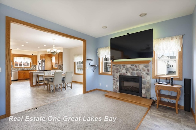 living area with a wealth of natural light, baseboards, a notable chandelier, and a fireplace