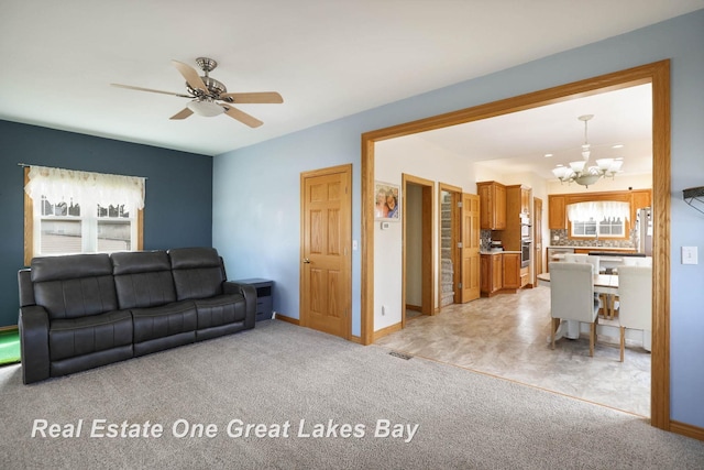 living room featuring visible vents, light carpet, a healthy amount of sunlight, and ceiling fan with notable chandelier