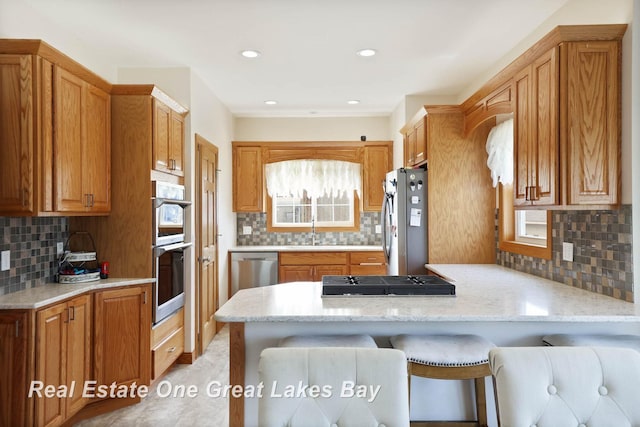 kitchen featuring tasteful backsplash, appliances with stainless steel finishes, a peninsula, brown cabinetry, and a sink