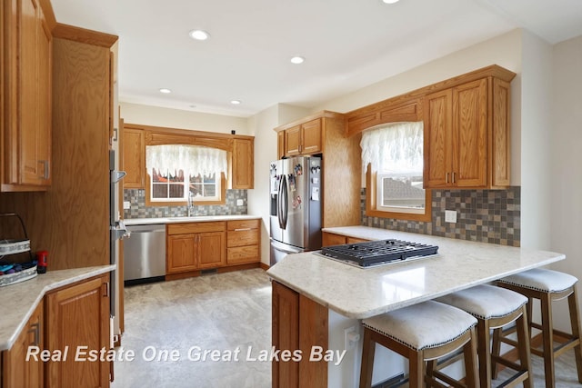 kitchen with a breakfast bar area, decorative backsplash, brown cabinets, a peninsula, and stainless steel appliances