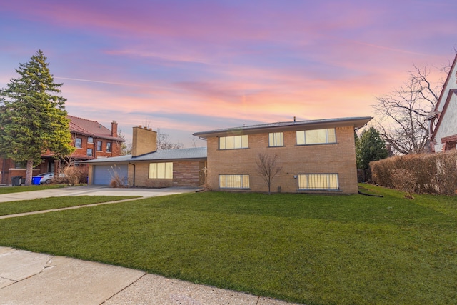 tri-level home featuring driveway, a yard, a garage, brick siding, and a chimney