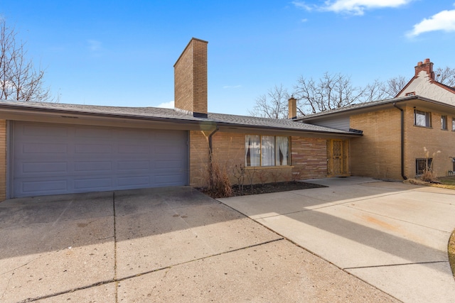 view of front of house featuring brick siding, driveway, an attached garage, and a chimney