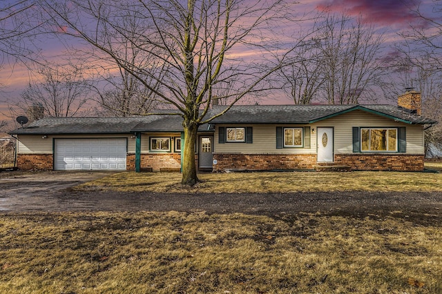 view of front of house featuring a front yard, driveway, a chimney, a garage, and brick siding