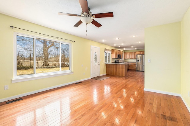 unfurnished living room featuring a sink, visible vents, baseboards, and light wood-style flooring