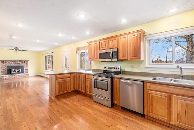 kitchen featuring light wood finished floors, open floor plan, appliances with stainless steel finishes, a peninsula, and a sink