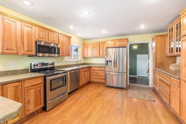 kitchen featuring a sink, recessed lighting, stainless steel appliances, light wood-style floors, and glass insert cabinets