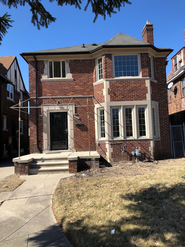 traditional home with a front lawn, fence, brick siding, and a chimney