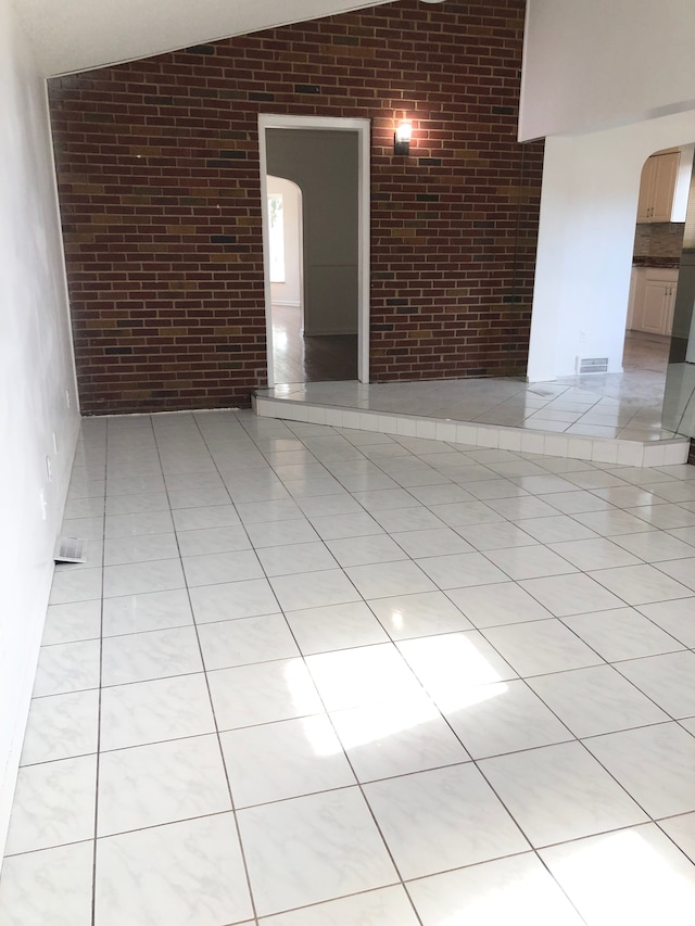 spare room featuring light tile patterned floors, visible vents, brick wall, lofted ceiling, and arched walkways