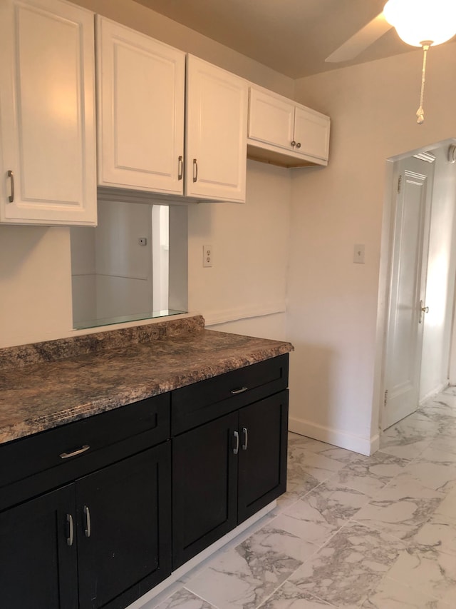 kitchen featuring marble finish floor, dark countertops, white cabinets, baseboards, and dark cabinets