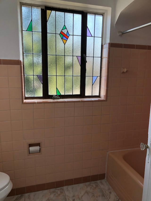 bathroom featuring toilet, tile walls, and wainscoting