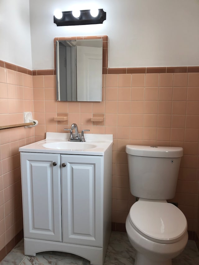 bathroom with vanity, a wainscoted wall, tile walls, toilet, and marble finish floor