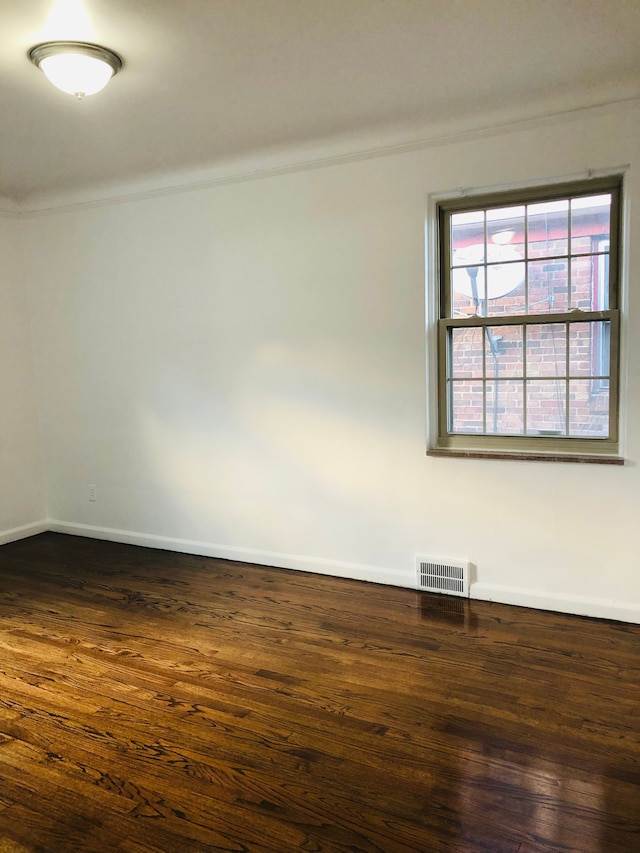 empty room with visible vents, dark wood-type flooring, and baseboards