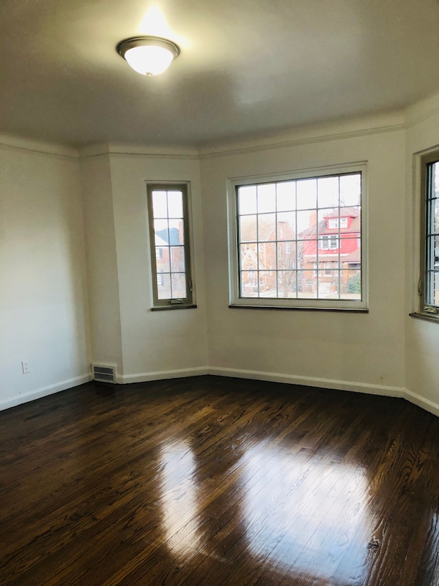 empty room with visible vents, dark wood-type flooring, baseboards, and ornamental molding