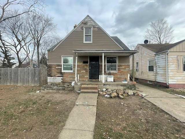 bungalow-style home with stone siding, a porch, and fence