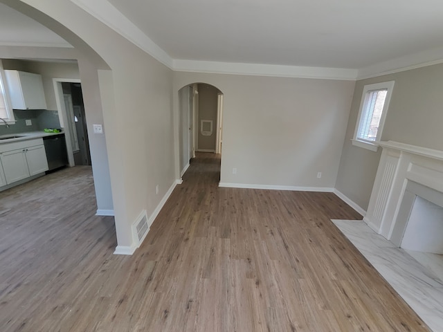 unfurnished living room with light wood-style flooring, ornamental molding, a sink, arched walkways, and baseboards