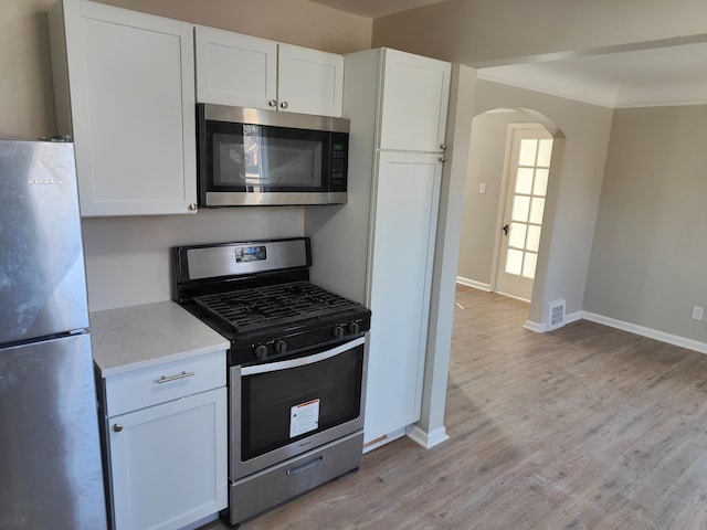 kitchen featuring arched walkways, white cabinets, stainless steel appliances, and light wood-type flooring